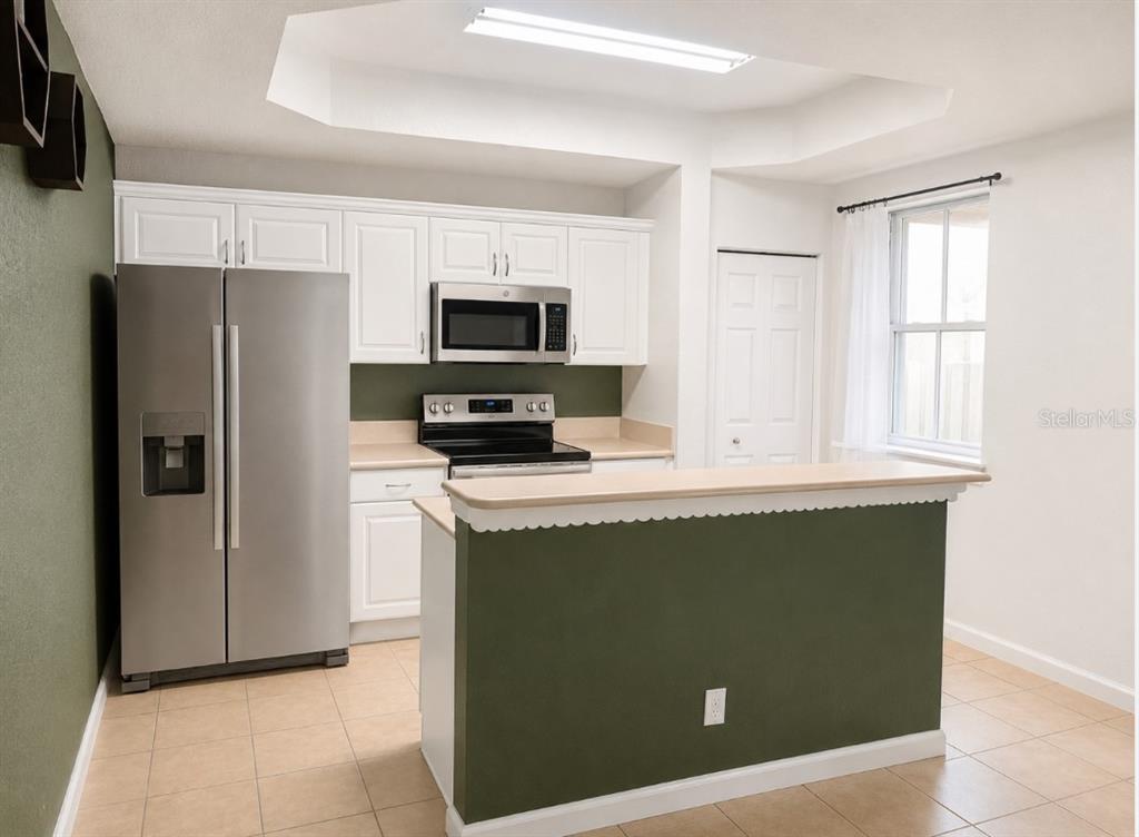 A kitchen features white cabinets, stainless steel appliances, a breakfast bar, and olive green walls — 2928 HIDDEN HILLS ROAD UNIT 1405, WEST PALM BEACH, FL