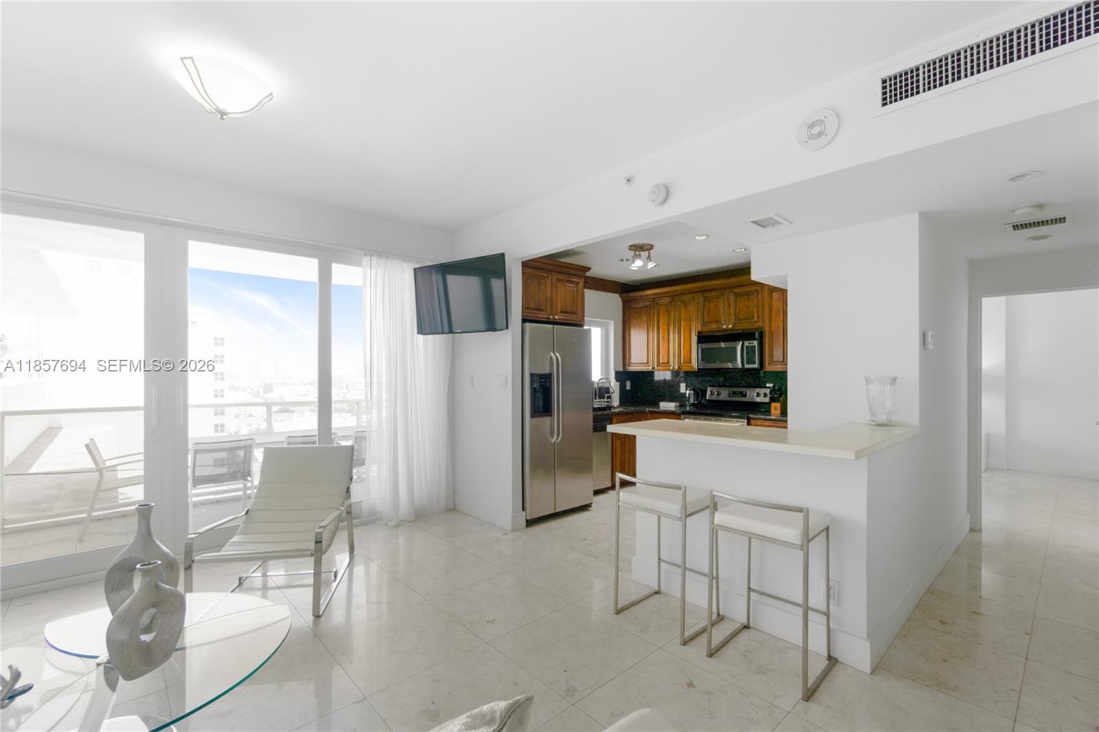 A bright living area features a kitchen with wood cabinets, a breakfast bar, and balcony access — 100 Lincoln Rd, Miami Beach FL 33139, MIAMI BEACH, FL