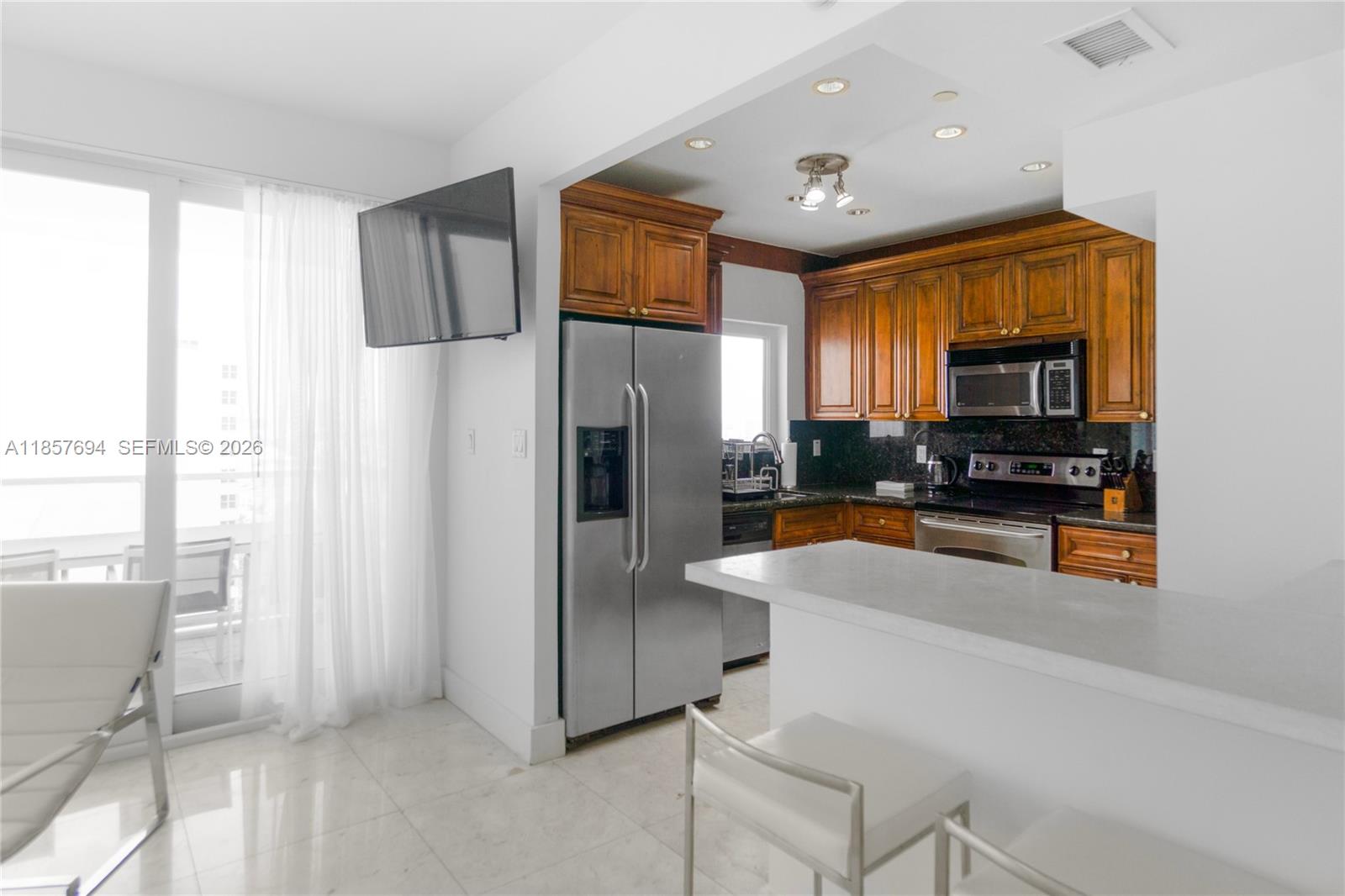 A kitchen features wood cabinets, stainless steel appliances, and a white breakfast bar — 100 Lincoln Rd, Miami Beach FL 33139, MIAMI BEACH, FL