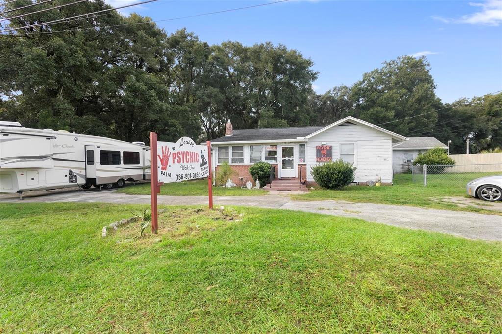 A white house with a psychic business sign stands on a grassy lot with a trailer — 2480 N WOODLAND BOULEVARD, DELAND, FL