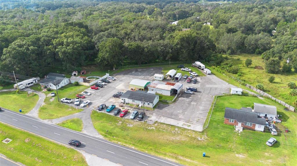 An aerial view shows a commercial property with multiple buildings, parking areas, and surrounding trees — 2480 N WOODLAND BOULEVARD, DELAND, FL