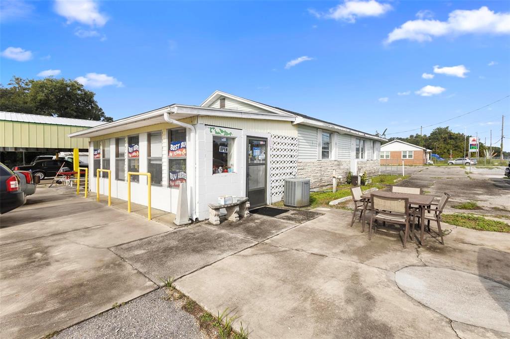 A single-story commercial building with a concrete patio, outdoor seating, and yellow metal bollards — 2480 N WOODLAND BOULEVARD, DELAND, FL