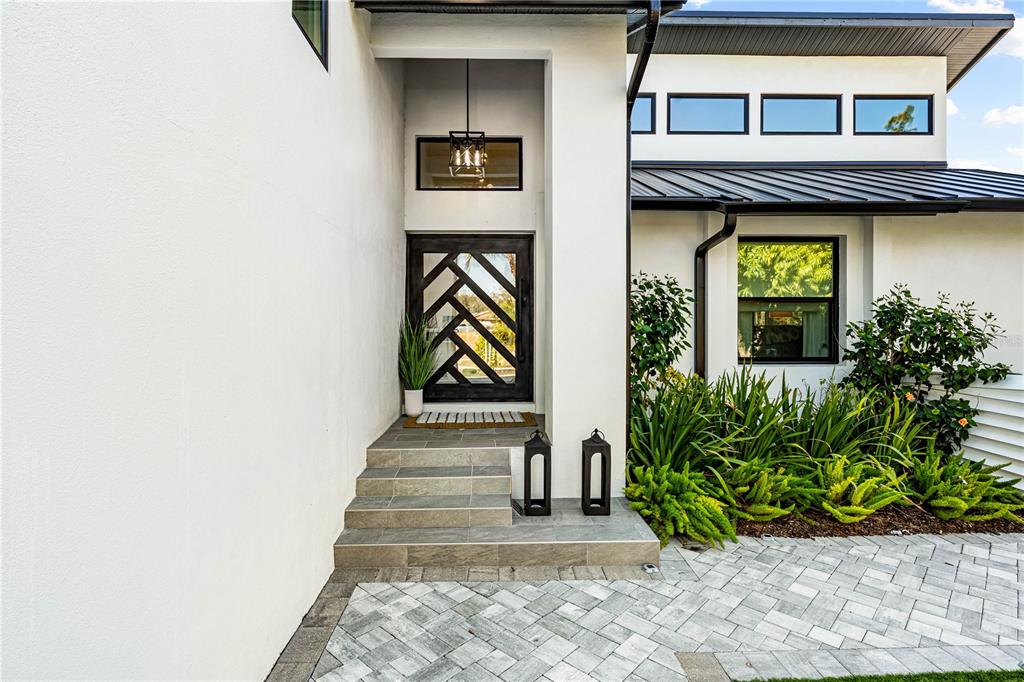 A modern home entrance features a geometric glass door, stone steps, and a paved walkway — 2500 MONTEREY STREET, SARASOTA, FL
