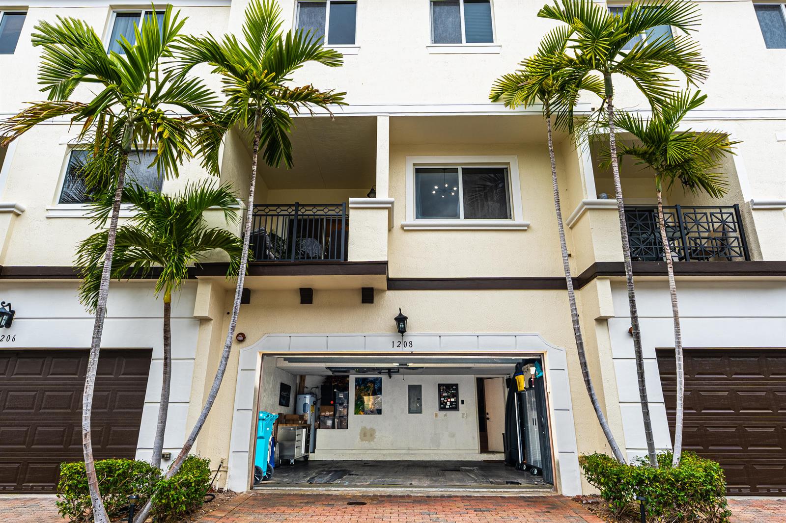 A three-story townhouse exterior features a ground-level open garage, two balconies, and palm trees — 1208 Coastal Bay Boulevard, Boynton Beach FL 33435, BOYNTON BEACH, FL