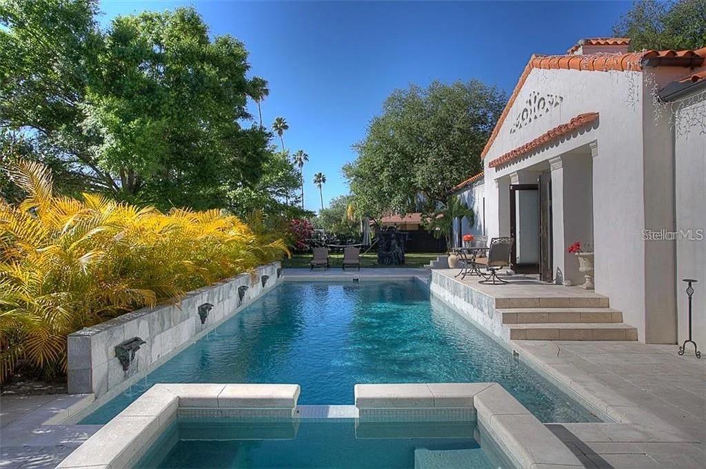A rectangular swimming pool and hot tub sit beside a white stucco house with palm trees — 100 W DAVIS BOULEVARD, TAMPA, FL