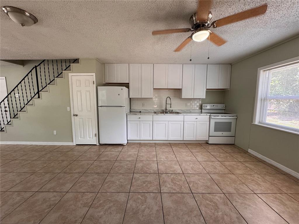 A kitchen with white cabinets, tile flooring, a ceiling fan, and a window — 538 ORANGE STREET UNIT 538, MASCOTTE, FL
