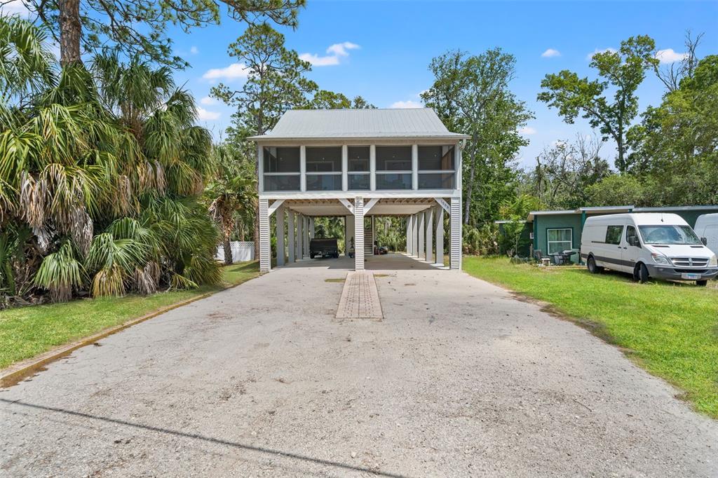 A stilt house with a screened-in porch stands above a gravel driveway and parking area — 1566 INDIAN BAY ROAD, SPRING HILL, FL