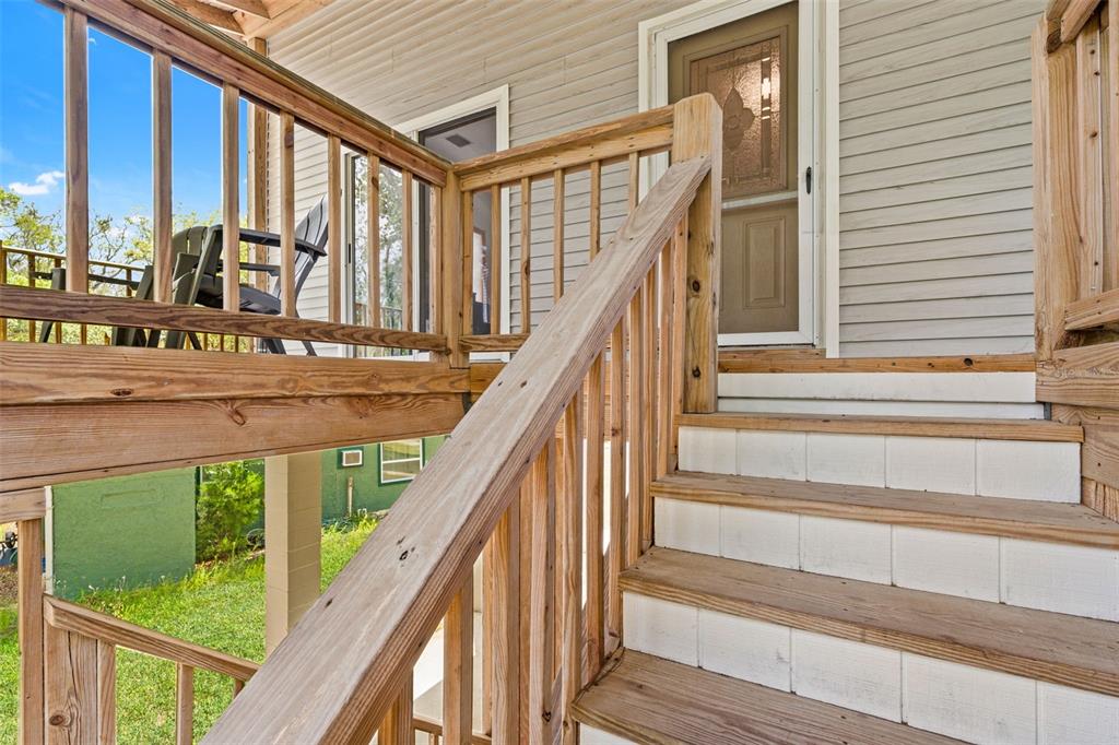 A wooden staircase with white risers leads to a deck and a house entrance — 1566 INDIAN BAY ROAD, SPRING HILL, FL