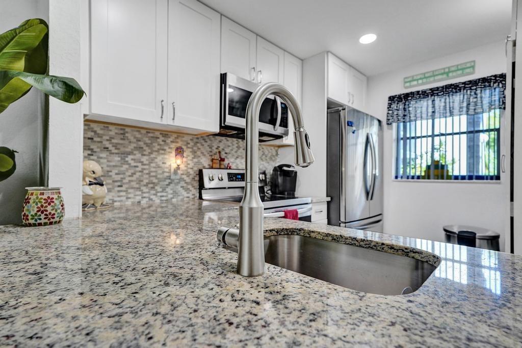 A kitchen features granite countertops, white cabinets, a stainless steel sink, and a stainless steel refrigerator — 3060 Holiday Springs Boulevard # 106, Margate FL 33063, MARGATE, FL