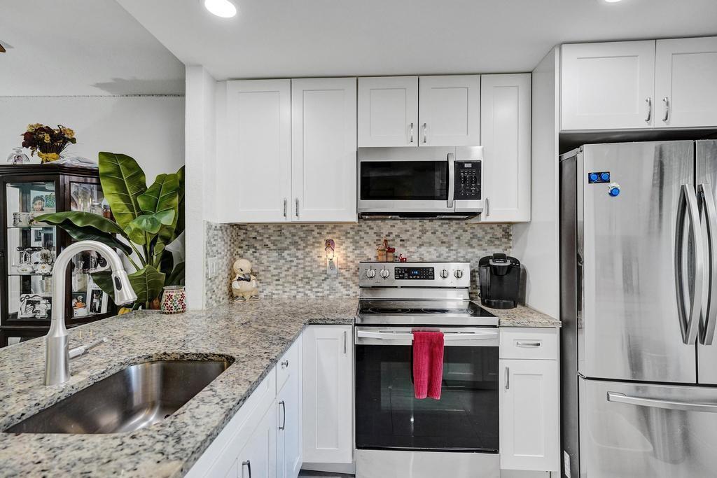 A kitchen features white cabinets, granite countertops, stainless steel appliances, and a mosaic tile backsplash — 3060 Holiday Springs Boulevard # 106, Margate FL 33063, MARGATE, FL