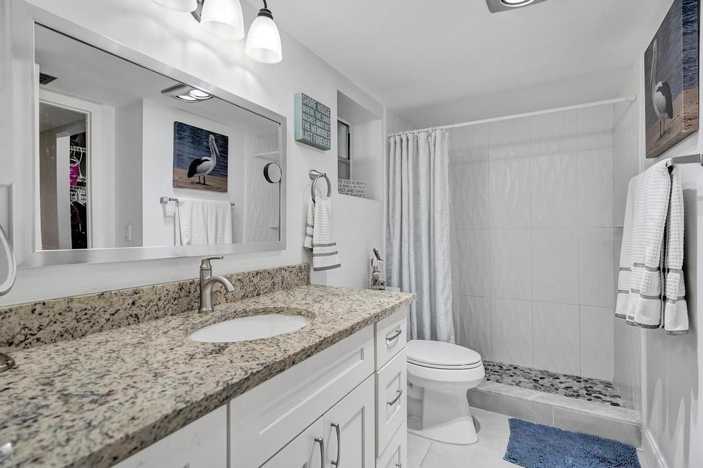 A bathroom features a granite vanity, white cabinets, a walk-in shower, and coastal-themed wall art — 3060 Holiday Springs Boulevard # 106, Margate FL 33063, MARGATE, FL