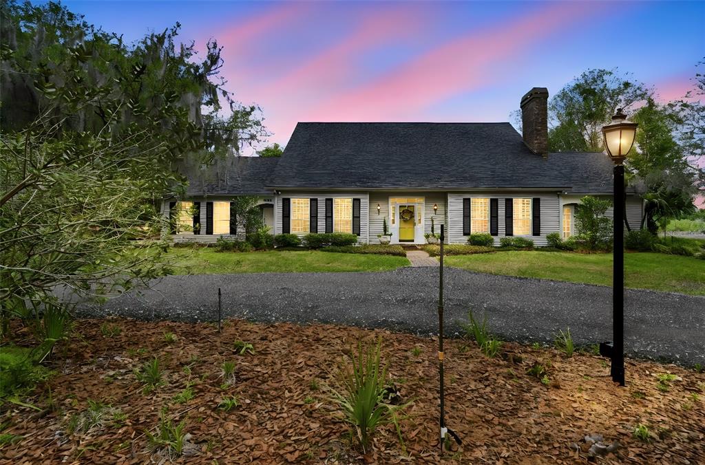 A single-story house with a dark roof, gray siding, and a yellow front door at dusk — 1245 WESTOAK DRIVE, DELAND, FL