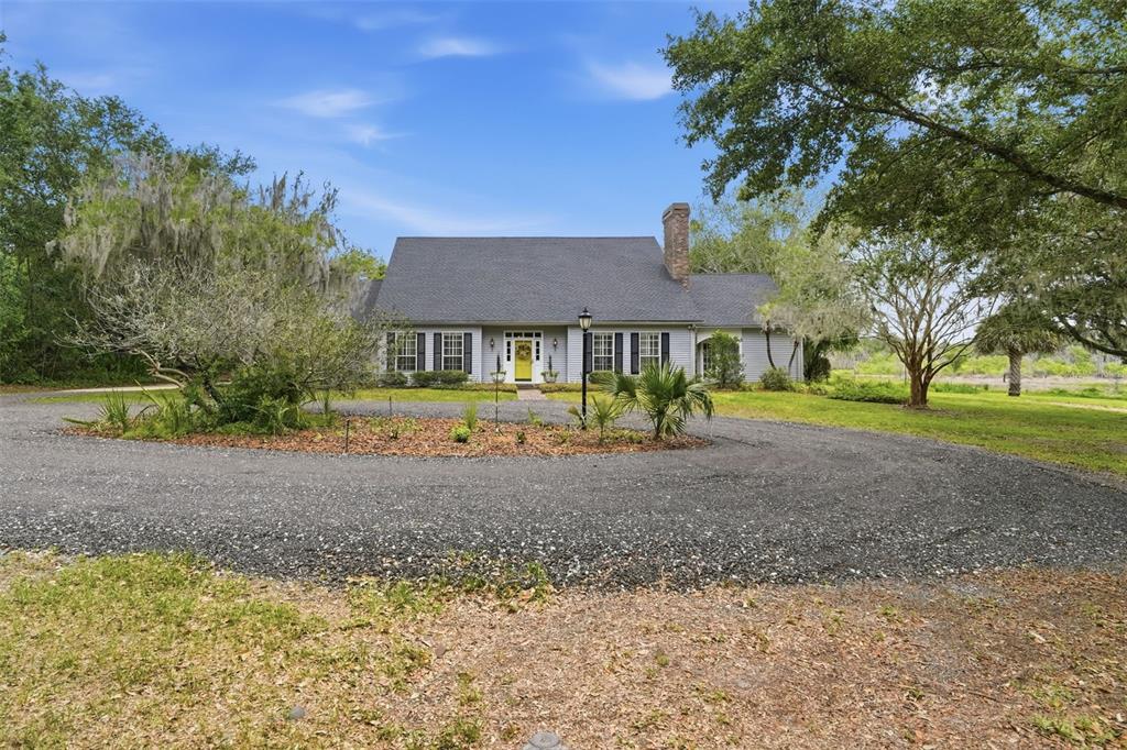 A gray house with a yellow front door sits behind a circular gravel driveway — 1245 WESTOAK DRIVE, DELAND, FL