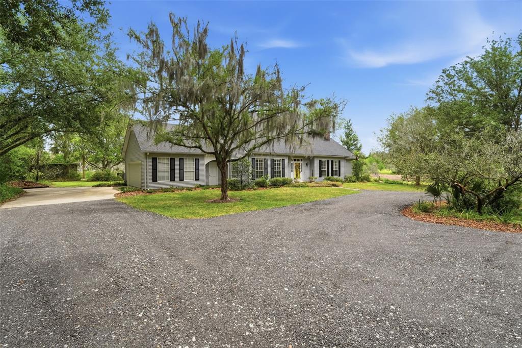A gray house with black shutters sits behind a large tree and gravel driveway — 1245 WESTOAK DRIVE, DELAND, FL