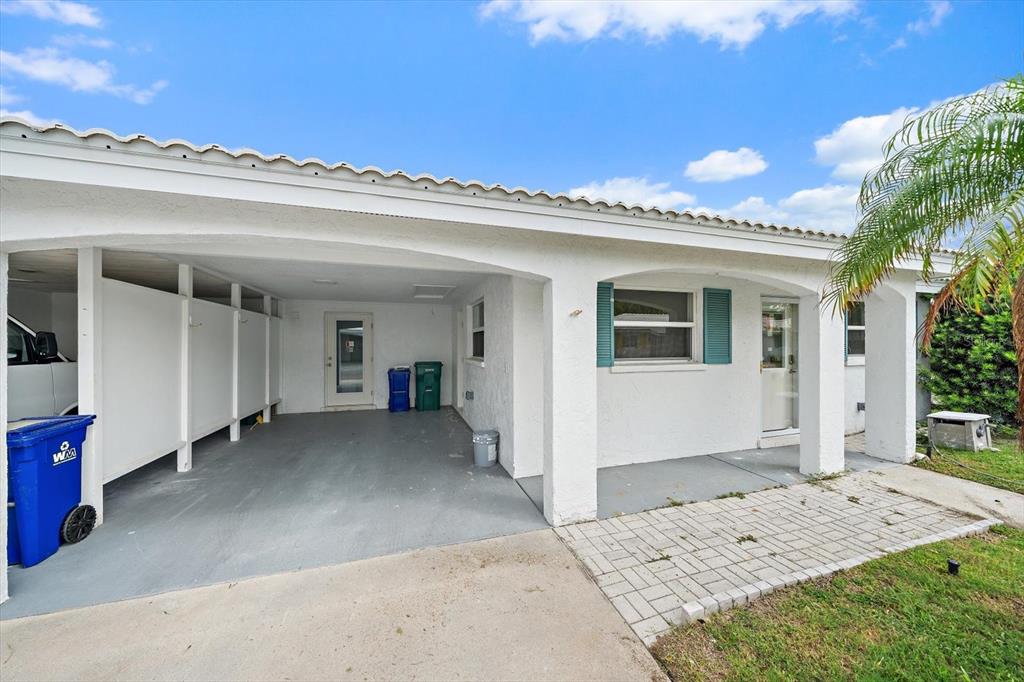 A white house exterior features a covered carport, a paved walkway, and teal window shutters — 683 SPANISH DRIVE S UNIT 214, LONGBOAT KEY, FL