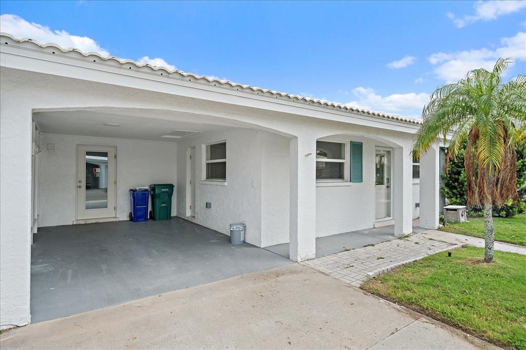 A white stucco house exterior features a covered carport, a paved walkway, and a palm tree — 683 SPANISH DRIVE S UNIT 214, LONGBOAT KEY, FL