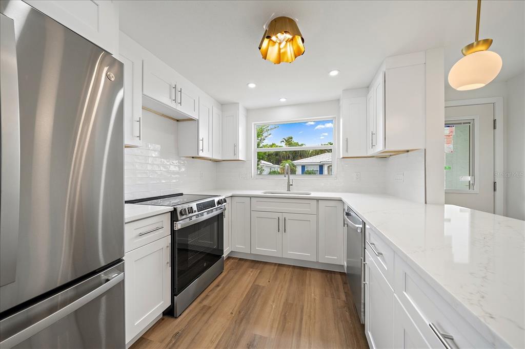 A modern kitchen features white cabinets, stainless steel appliances, white countertops, and wood-look flooring — 683 SPANISH DRIVE S UNIT 214, LONGBOAT KEY, FL