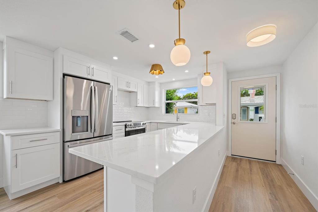 A modern kitchen features white cabinets, stainless steel appliances, a quartz island, and pendant lighting — 683 SPANISH DRIVE S UNIT 214, LONGBOAT KEY, FL