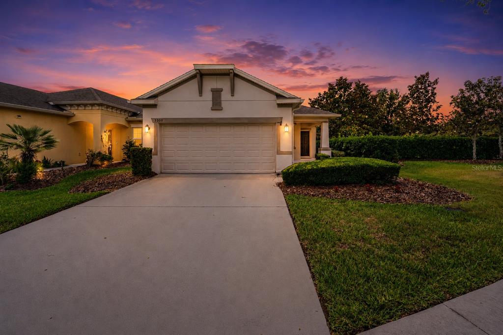 A single-story house with a two-car garage and a concrete driveway at sunset — 3300 SAGEBRUSH STREET, HARMONY, FL