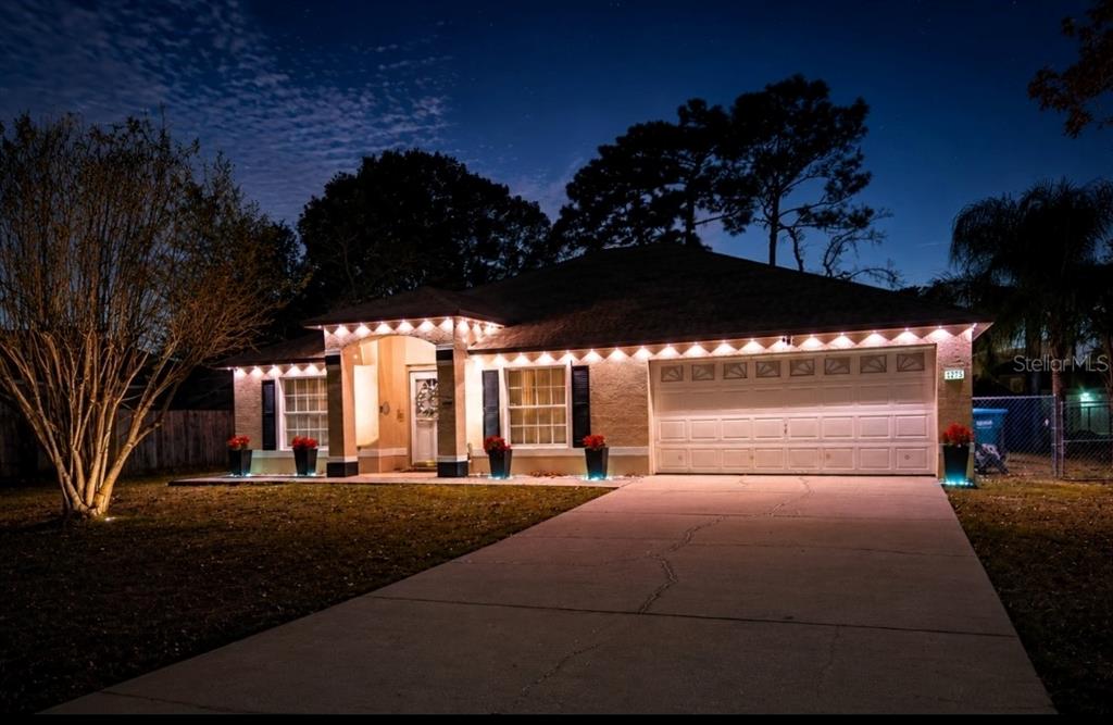 A single-story house with a concrete driveway and exterior accent lighting at night — 1779 MEREDITH AVENUE, DELTONA, FL