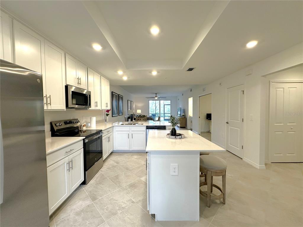 A modern kitchen features white cabinetry, stainless steel appliances, a center island, and tile flooring — 14221 HERITAGE LANDING BOULEVARD UNIT 2017, PUNTA GORDA, FL
