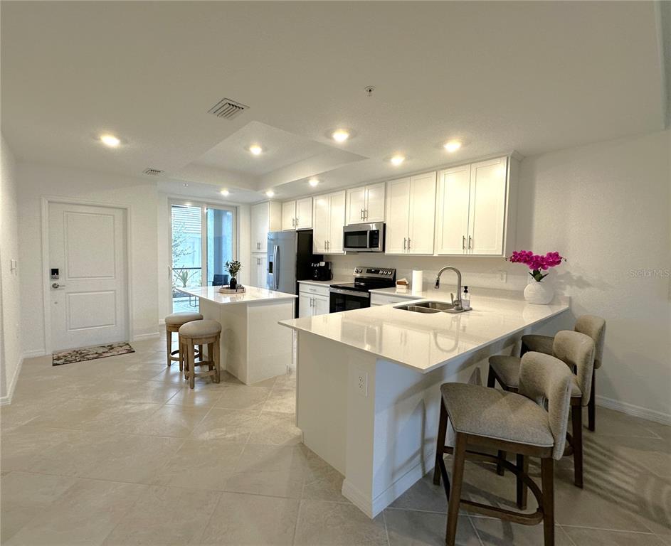 A modern kitchen features white cabinetry, quartz countertops, a center island, and tile flooring — 14221 HERITAGE LANDING BOULEVARD UNIT 2017, PUNTA GORDA, FL