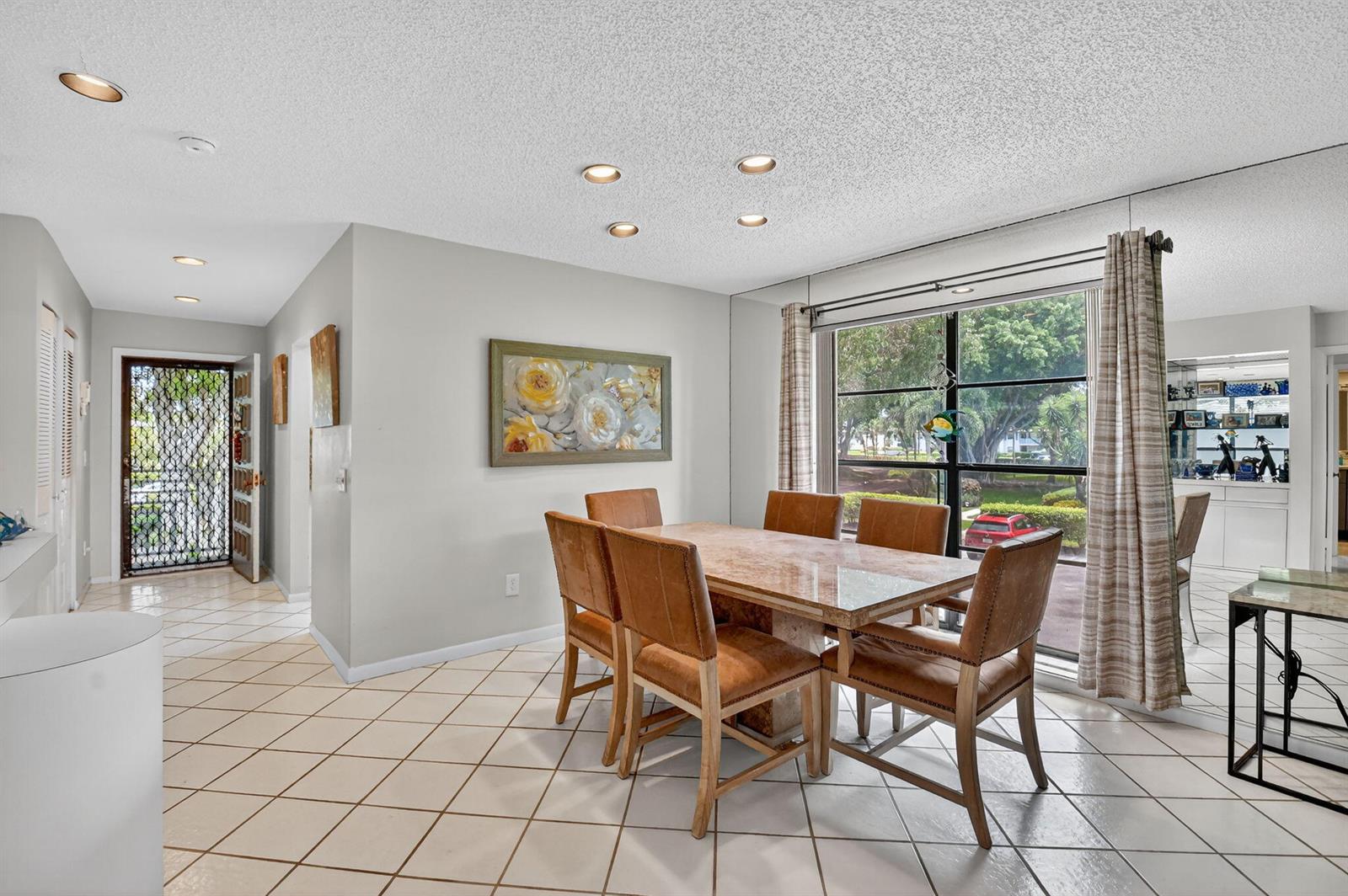 A dining room with a stone table, leather chairs, tiled floors, and a large window — 7 Southport Lane # B, Boynton Beach FL 33436, BOYNTON BEACH, FL