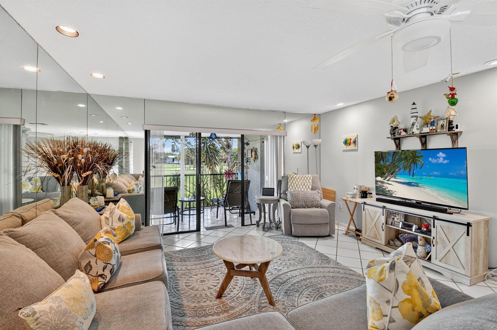 A living room features a sectional sofa, a round coffee table, and a mirrored wall — 7 Southport Lane # B, Boynton Beach FL 33436, BOYNTON BEACH, FL