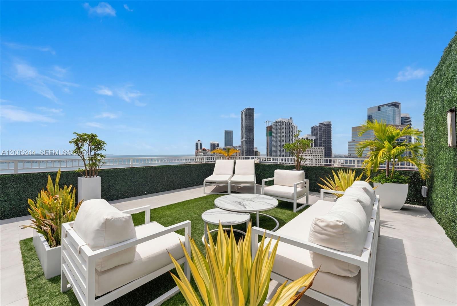 A rooftop terrace features white outdoor furniture, artificial grass, potted plants, and a city skyline view — 801 Brickell Key Blvd, Miami FL 33131, MIAMI, FL