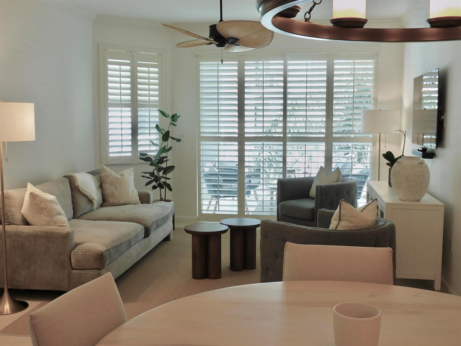A living room features a gray sofa, two armchairs, wooden side tables, and plantation shutters — 815 NW Flagler Avenue # 302, Stuart FL 34994, STUART, FL