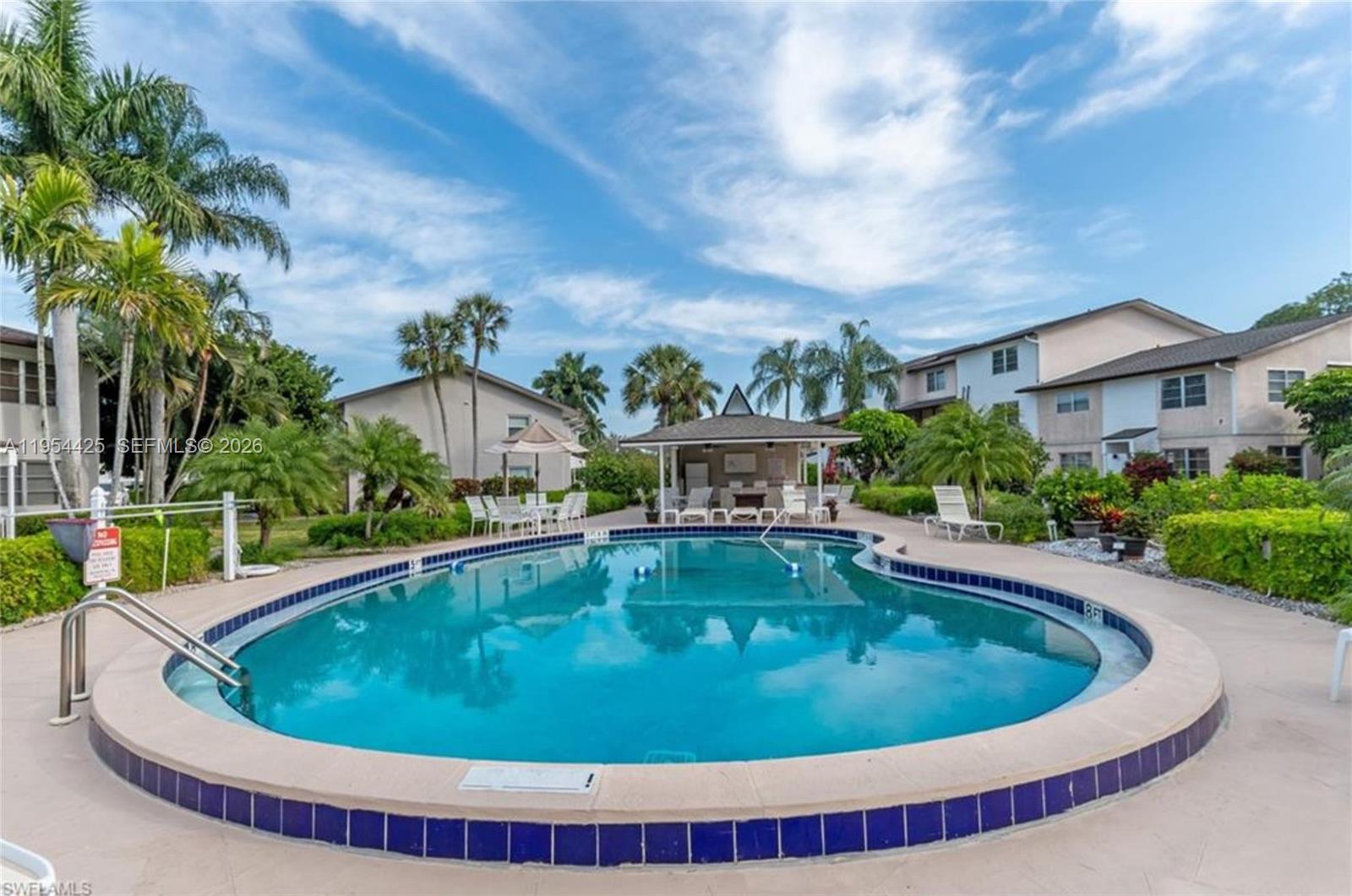A kidney-shaped swimming pool sits in a courtyard surrounded by palm trees and apartment buildings — 180 E Cypress Way # E230, Naples FL 34110, NAPLES, FL
