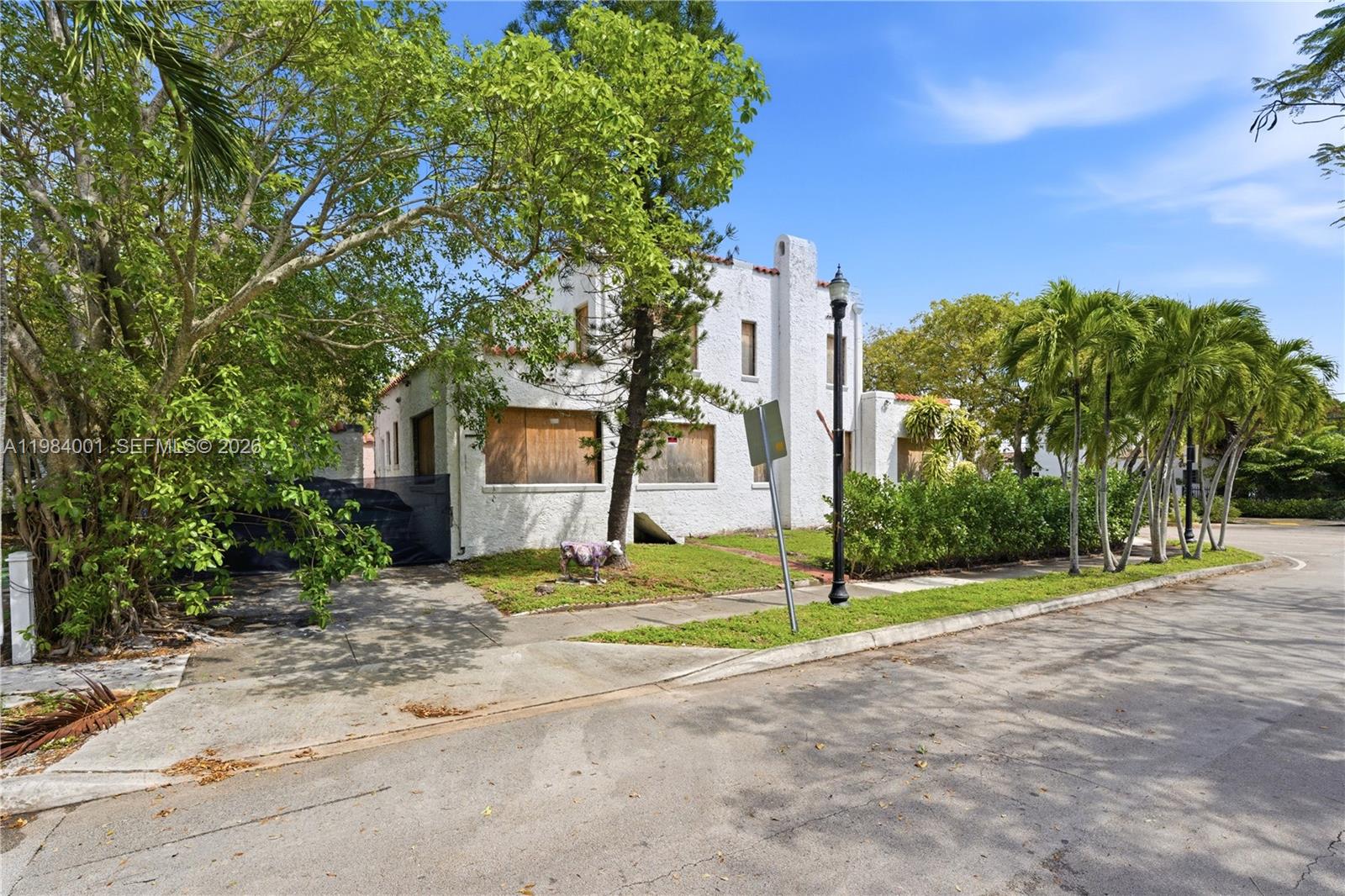 A white stucco house with boarded-up windows stands on a corner lot with palm trees — 4400 NE 1st Ave, Miami FL 33137, MIAMI, FL