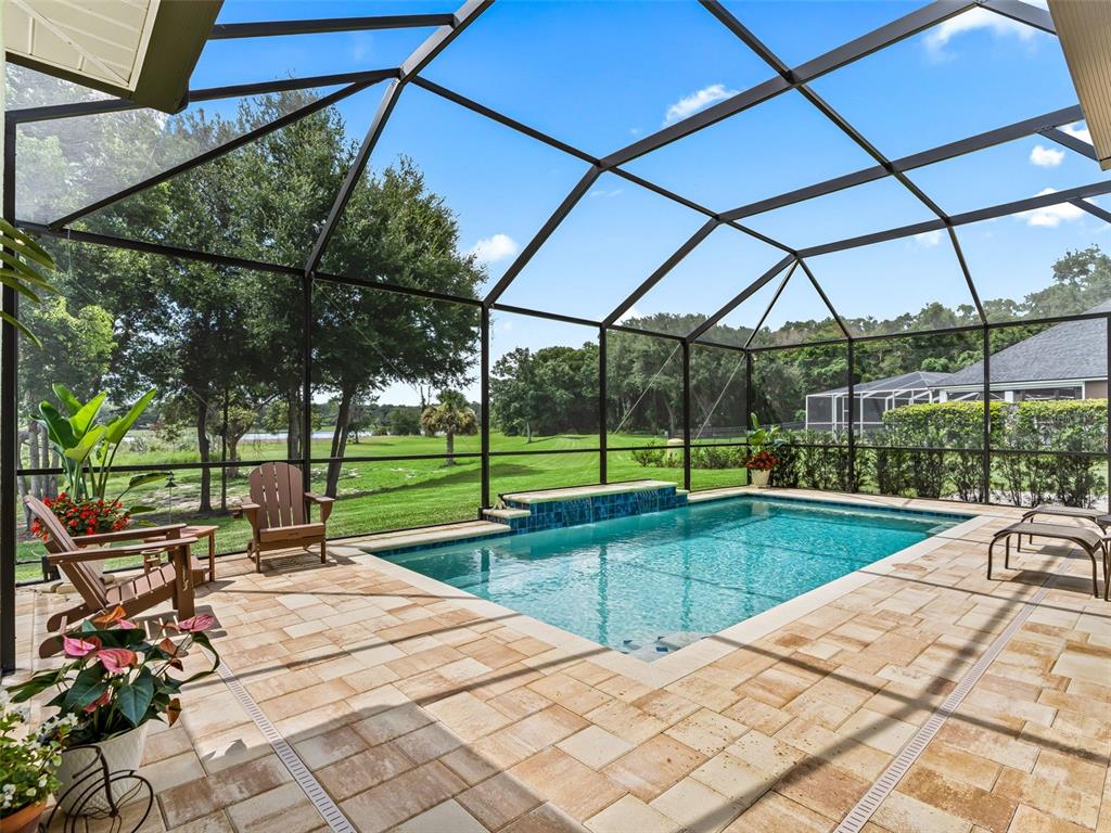 A screened-in patio features a rectangular swimming pool with a tiled water feature and pavers — 3828 OAK POINTE DRIVE, LADY LAKE, FL