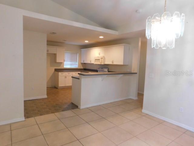 A kitchen with white cabinets and a breakfast bar overlooks a tiled dining area — 3034 BROCKTON STREET, NORTH PORT, FL