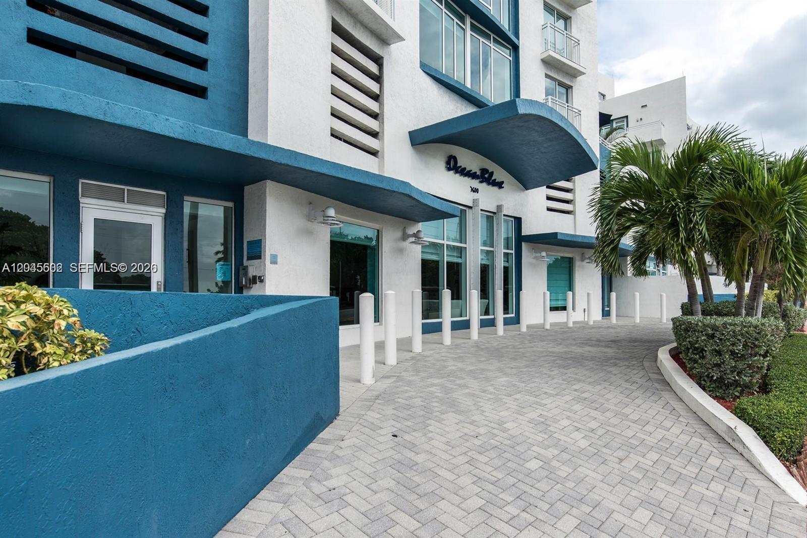 The exterior of a white and blue building features a paved driveway and palm trees — 7600 Collins Ave # 712, Miami Beach FL 33141, MIAMI BEACH, FL