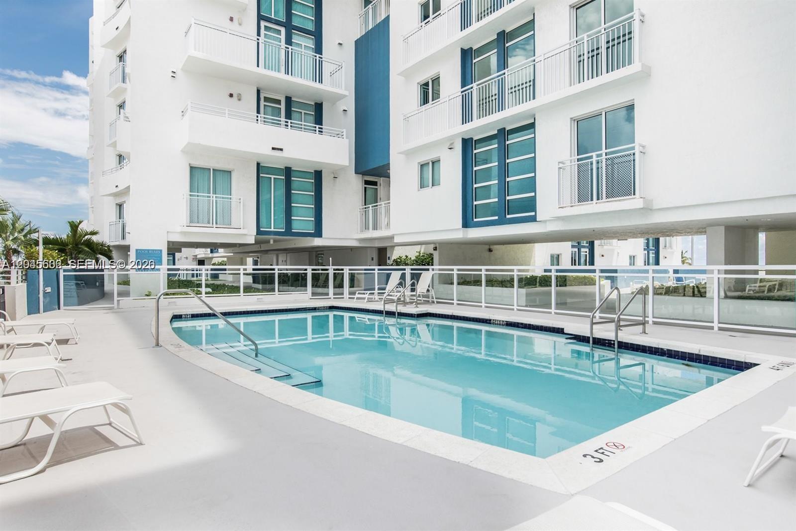 A swimming pool sits on a concrete deck in front of a multi-story white building — 7600 Collins Ave # 712, Miami Beach FL 33141, MIAMI BEACH, FL