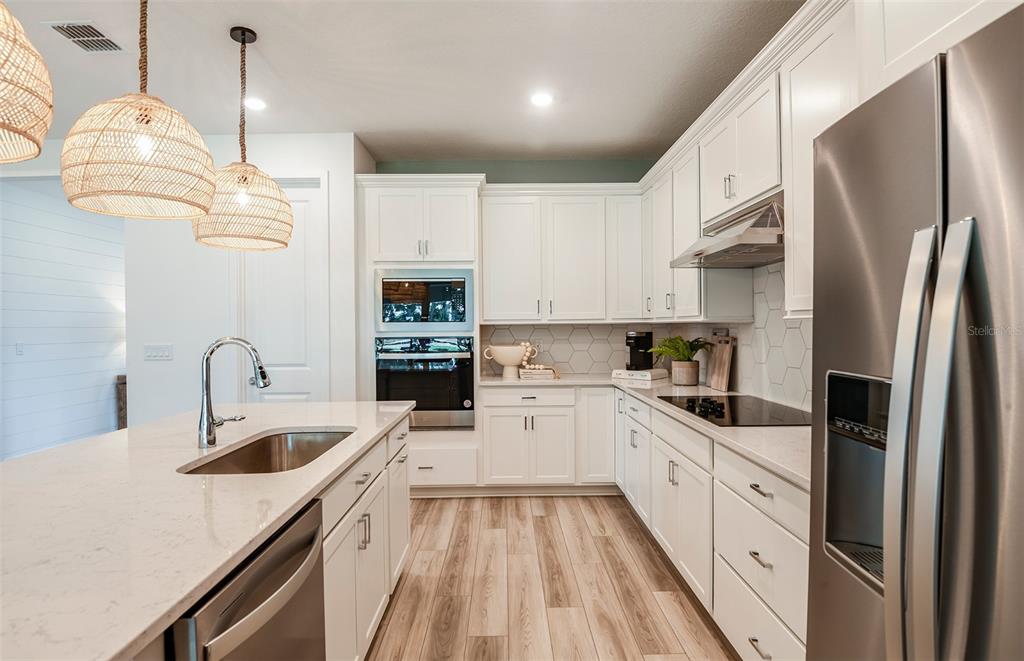 A modern kitchen features white cabinets, stainless steel appliances, a quartz island, and woven pendant lights — 37385 GUNNISON DRIVE, ZEPHYRHILLS, FL