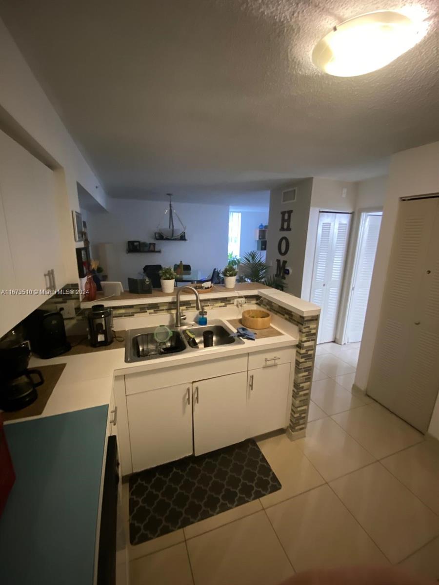 A kitchen with white cabinets, a double sink, and a tiled backsplash overlooks a dining area — 4440 NW 107th Ave # 7, Doral FL 33178, DORAL, FL