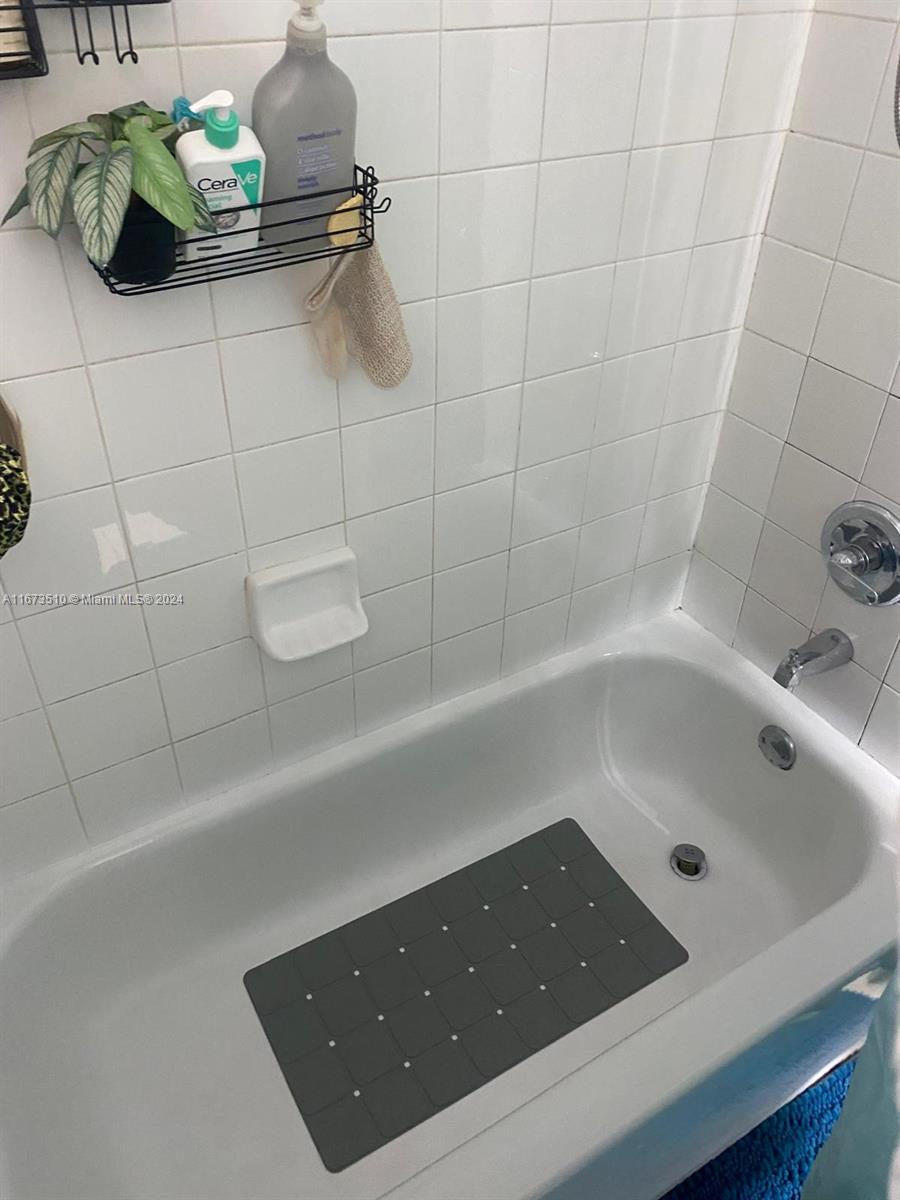 A white tiled bathtub area features a black wire shower caddy and a gray mat — 4440 NW 107th Ave # 7, Doral FL 33178, DORAL, FL