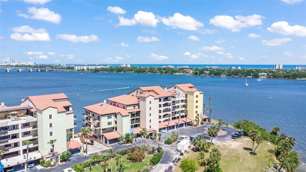 An aerial view shows a multi-story apartment complex situated along a waterfront with a bridge — 761 MARINA POINT DRIVE UNIT 7610, DAYTONA BEACH, FL