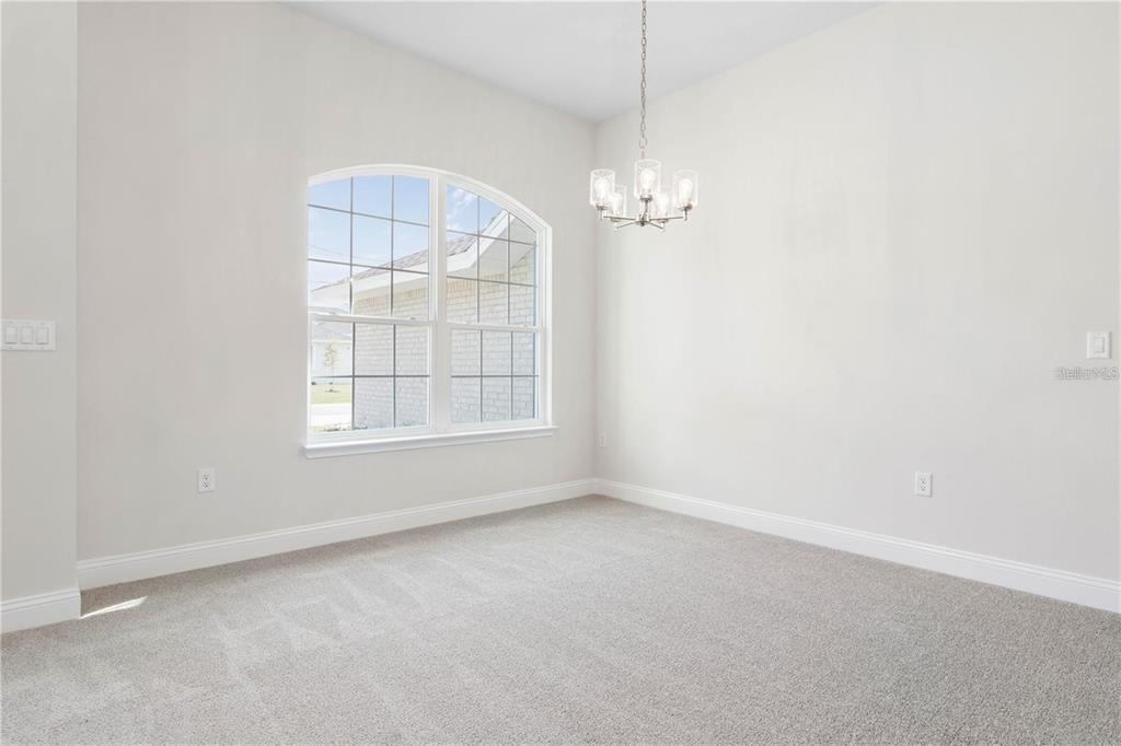 An empty dining room features light gray carpet, white walls, and an arched window — 39 BIRCHWOOD DRIVE, PALM COAST, FL