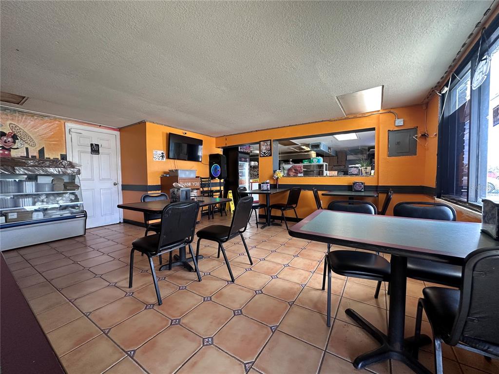 A small restaurant dining area features orange walls, tiled floors, and several tables with chairs — 9852 E COLONIAL DRIVE, ORLANDO, FL