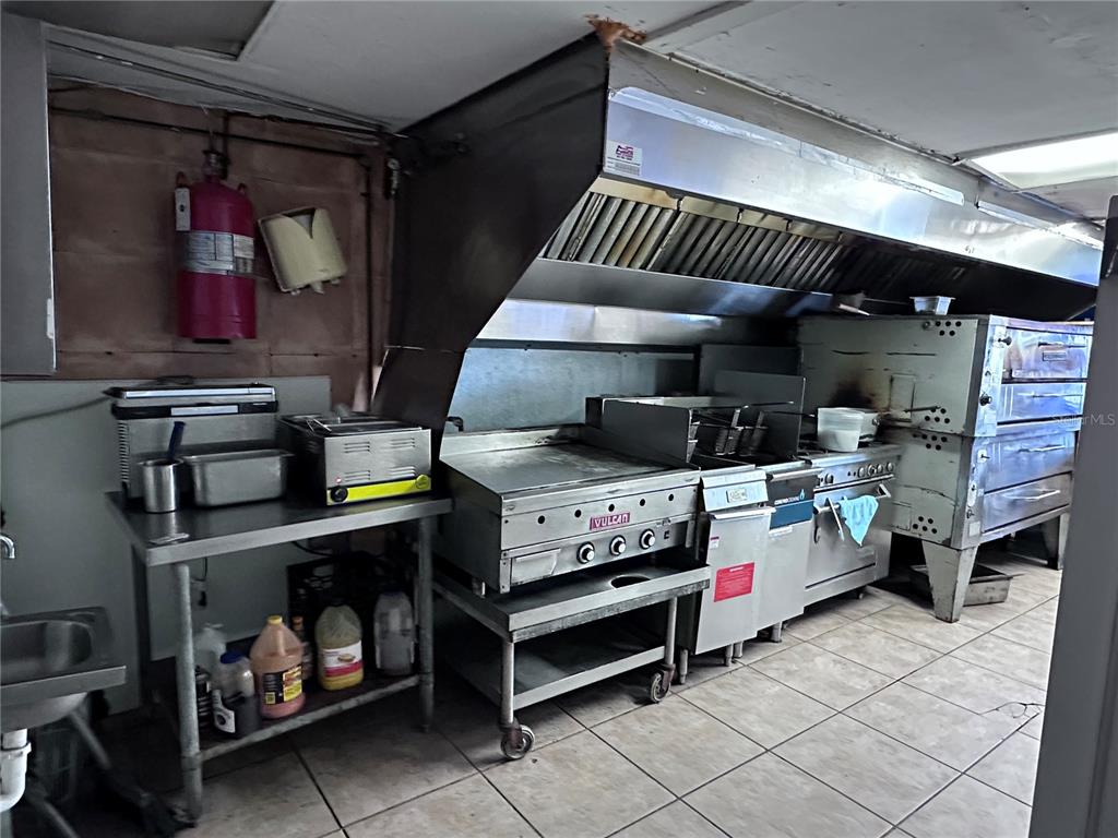 A commercial kitchen features stainless steel appliances, a large ventilation hood, and tile flooring — 9852 E COLONIAL DRIVE, ORLANDO, FL
