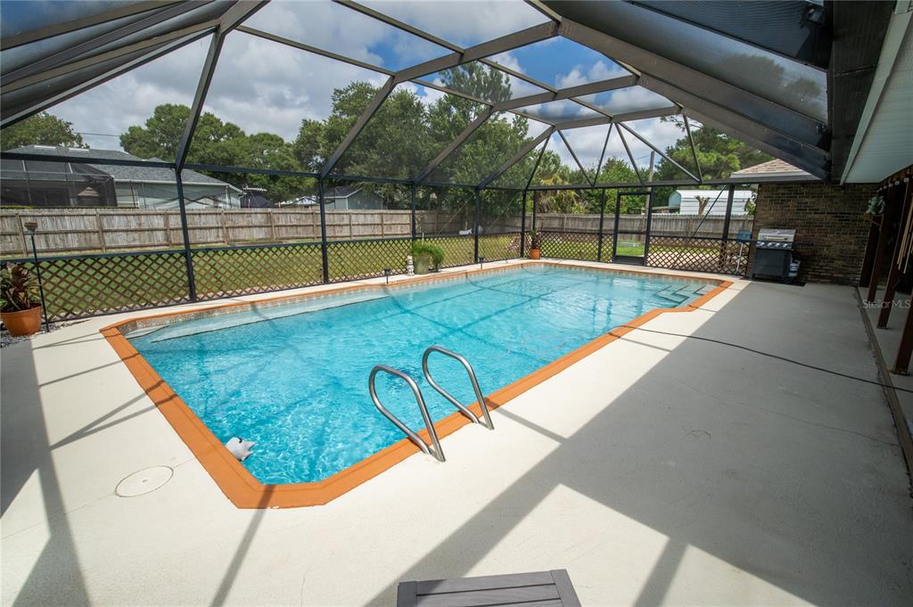 A rectangular swimming pool with a metal ladder sits inside a screened-in patio enclosure — 751 VEGA COURT NE, PALM BAY, FL