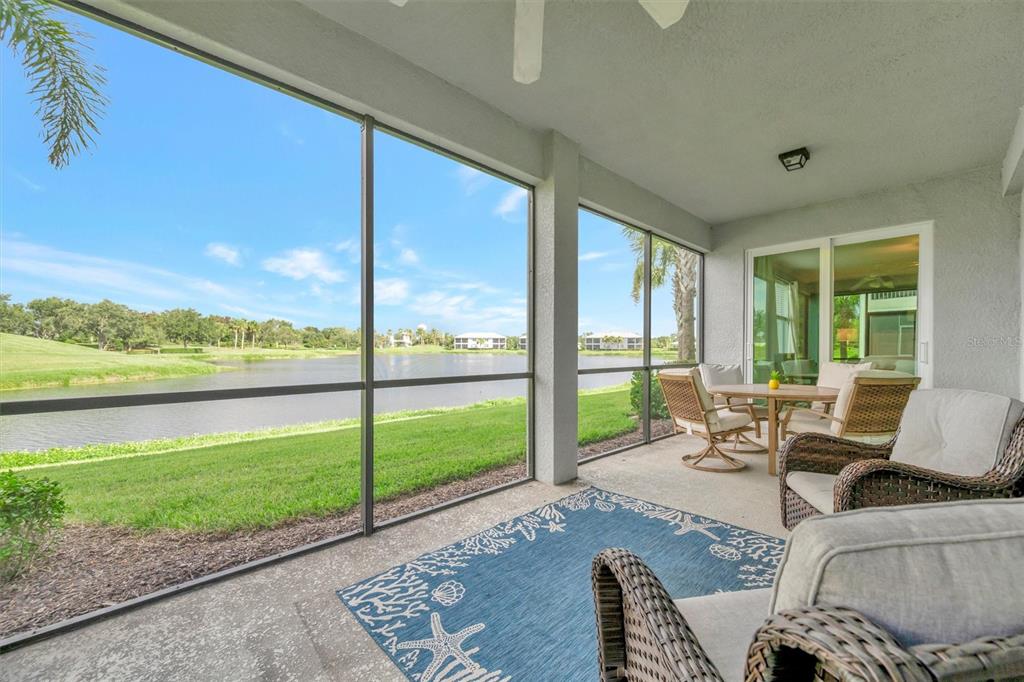 A screened-in patio features wicker furniture, a blue patterned rug, and views of a lake — 947 TIDEWATER SHORES LOOP, BRADENTON, FL