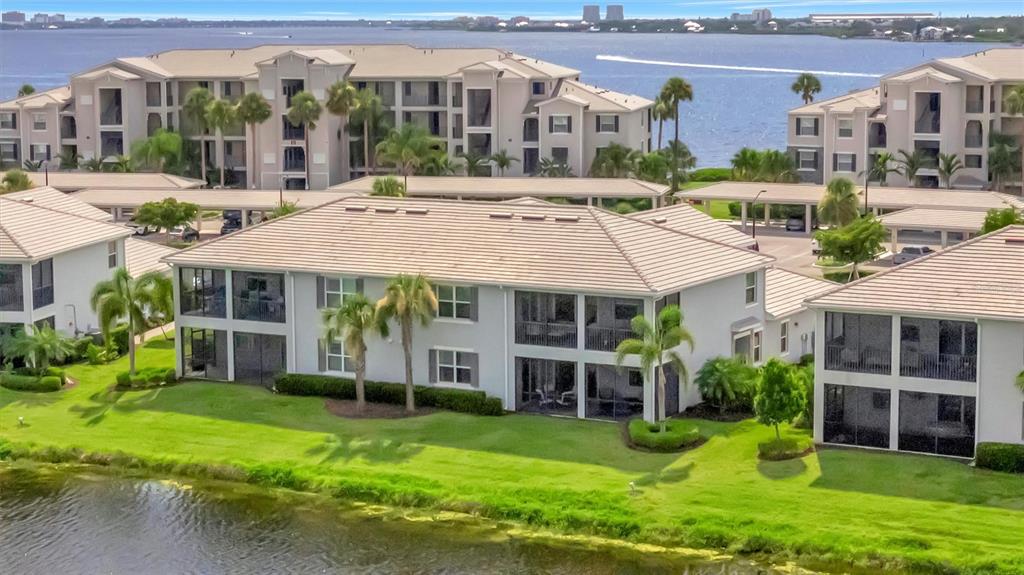 An aerial view shows multi-story apartment buildings with tiled roofs near a waterfront — 947 TIDEWATER SHORES LOOP, BRADENTON, FL