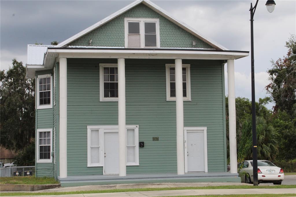 A two-story green house with a front porch, white columns, and a gabled roof — 1317 MAIN STREET, LEESBURG, FL