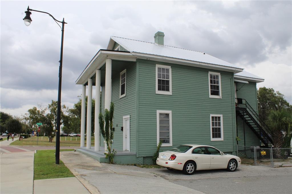 A two-story green house with white columns and a metal roof sits on a corner — 1317 MAIN STREET, LEESBURG, FL