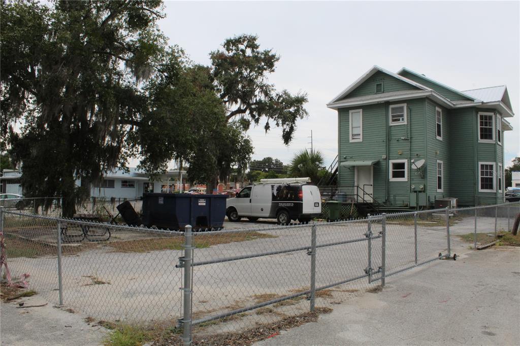 A green two-story house stands behind a chain-link fence with a white van parked nearby — 1317 MAIN STREET, LEESBURG, FL