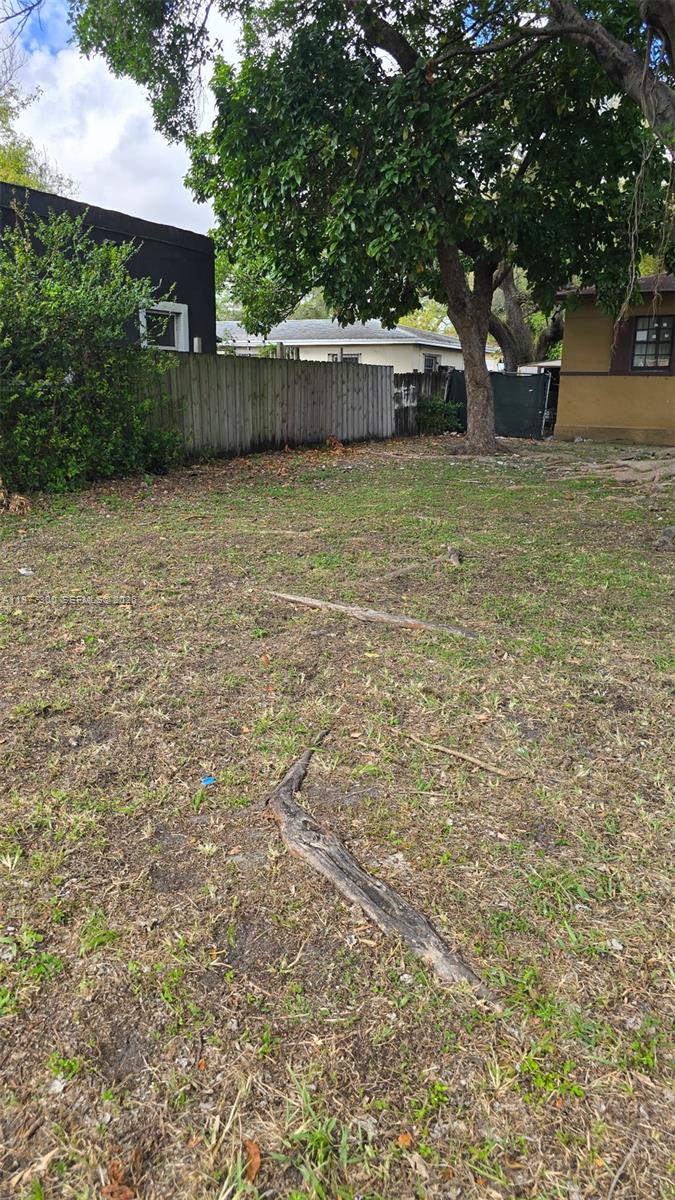 A grassy, partially shaded residential lot features exposed tree roots and a wooden fence — 6910 NW 5th Pl, Miami FL 33150, MIAMI, FL